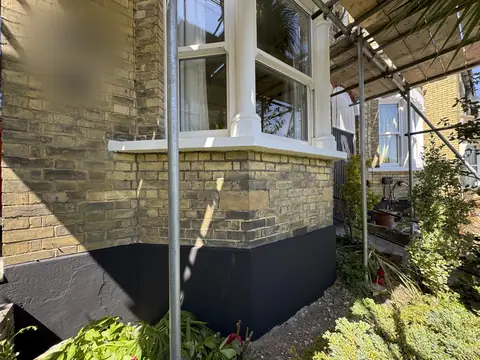 Ground floor bay with white sill and columns above yellow brick and a black painted plinth