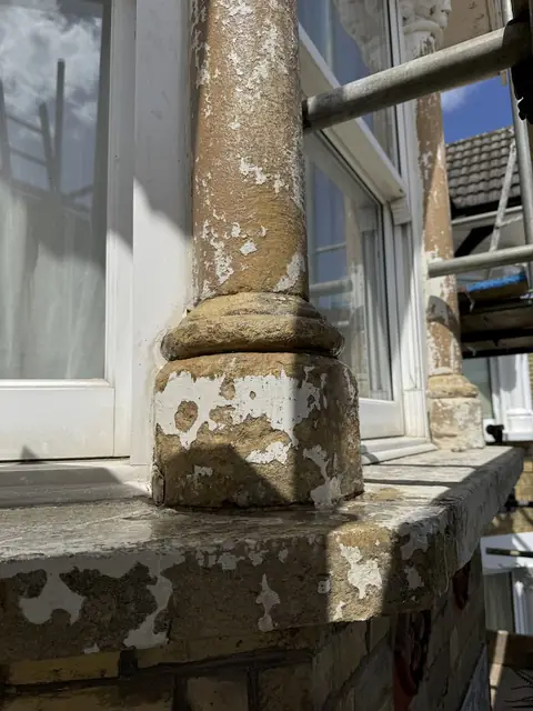 Bay window column base and sill scraped back to bare stone, with patches of old white paint left