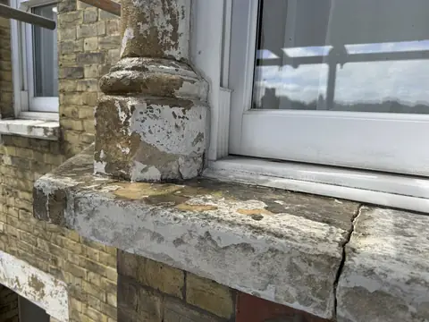 Bay window sill and column base scraped back to bare stone, with an open crack across the sill