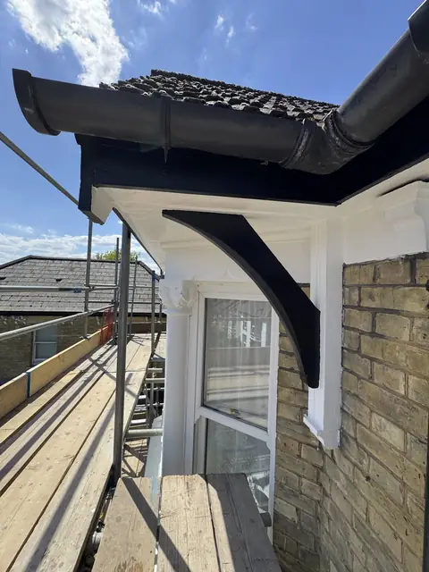 Black painted bracket and fascia under a gutter, with white soffit and white bay capitals