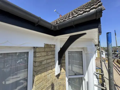 Corner of a bay roof with black fascia, gutter and bracket over a white soffit and cornice