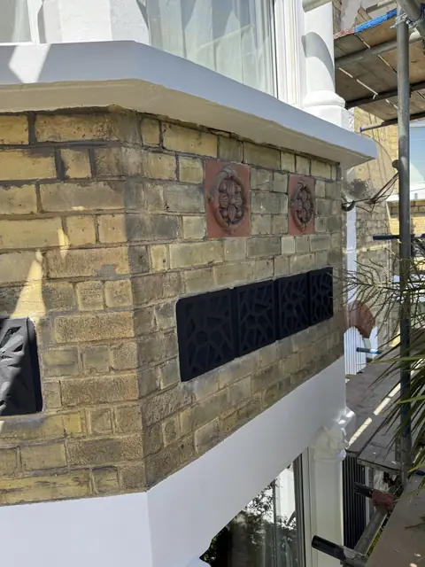 Yellow brick bay apron with two terracotta rosette tiles and four black pierced panels under a white sill