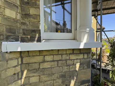 Bay window sill and column base painted white above yellow stock brick, scaffold to the right