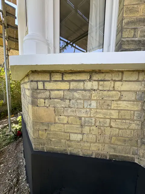 White bay sill and column base above yellow stock brick with a black painted plinth below