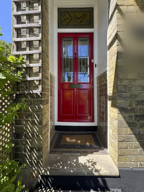 Glossy red front door with leaded glass and a stained glass fanlight in a tiled Victorian porch