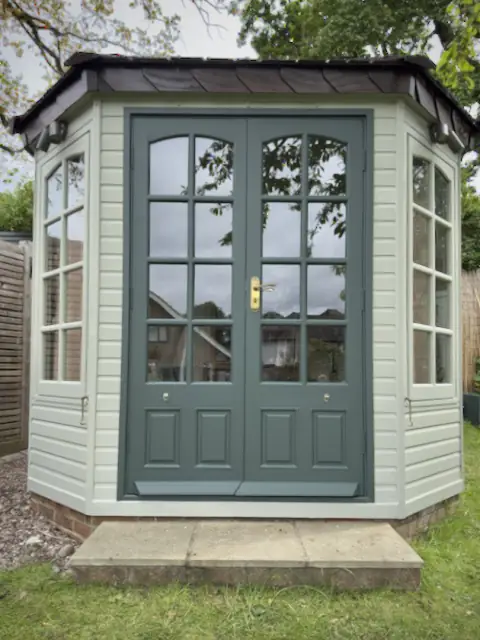 Garden office front after painting, pale grey-green weatherboard and dark green glazed double doors with brass handle