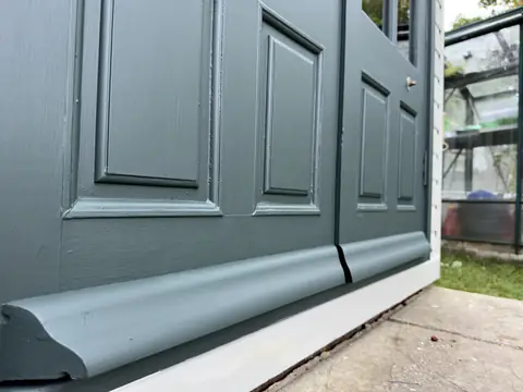Low-angle view along painted dark green garden office doors and the new drip bead at their base