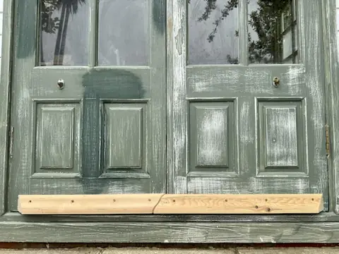 Sanded green garden office doors with bare timber weather strips newly fixed across the bottom of both doors
