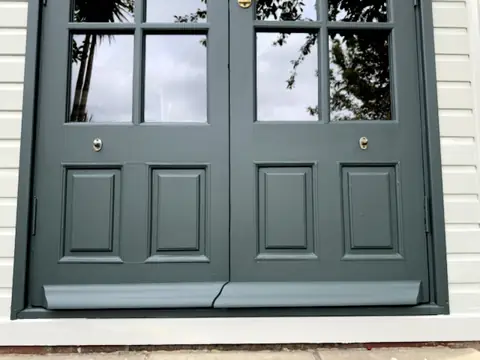 Lower half of garden office double doors painted dark green, new weather strips painted, pale grey-green boards beside