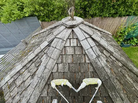 Weathered grey cedar shingle roof with moss and a broken finial at the apex, seen from above with a ladder stand-off