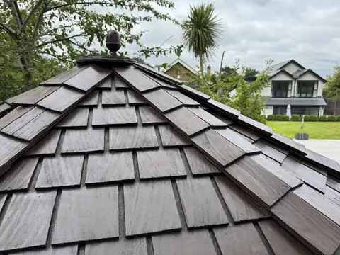 Cedar shingle roof stained dark brown with a new acorn finial, palm tree and a house in the background
