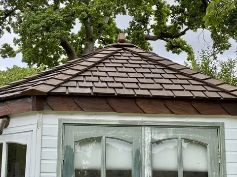 Garden office roof stained brown with a new acorn finial while the green doors below are still unpainted