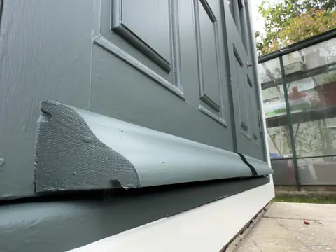 Close view of the profiled end of a painted weather strip at the base of a dark green door