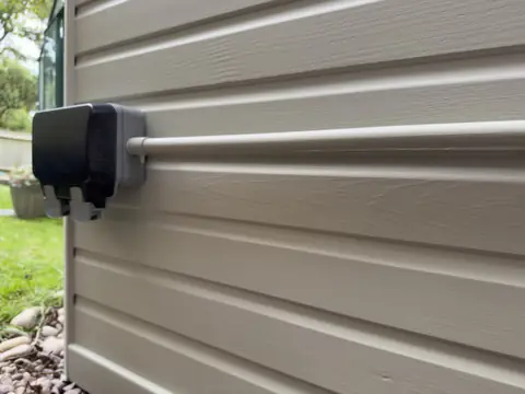 Black outdoor socket on painted weatherboard with the cable conduit painted to match the boards