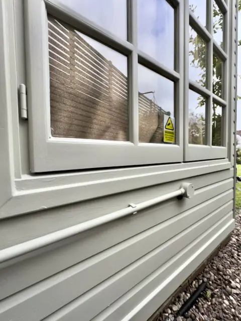 Pale grey-green window frame and weatherboard with a painted conduit run below the window