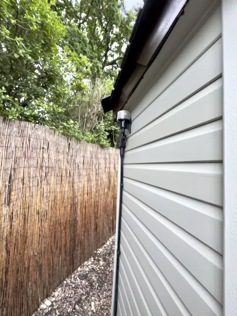 Narrow side of the garden office in pale painted weatherboard beside a tall reed screen fence