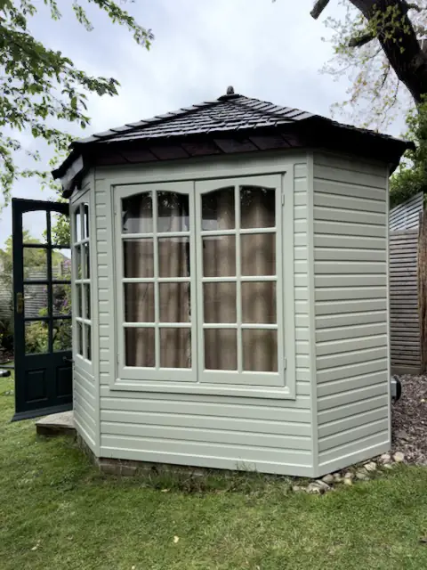 Garden office side with large glazed window, pale grey-green weatherboard, dark roof and open green door