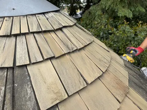 Close-up of timber roof shingles part sanded, with a gloved hand holding an electric sander