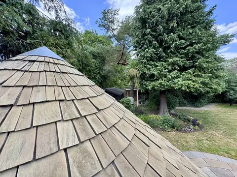 Sanded timber shingle roof of a circular gazebo with trees and a lawn beyond