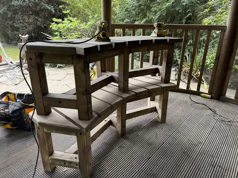 Timber bench turned upside down on another bench on gazebo decking, with two sanders on top