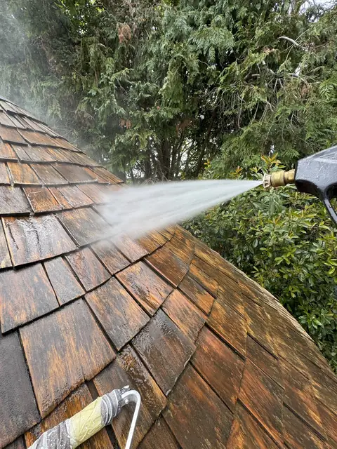 Pressure washer lance spraying water across the timber shingles of a gazebo roof
