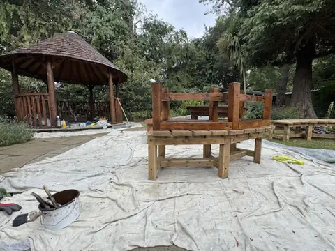 Varnished bench upside down on another bench on dust sheets, with the varnished gazebo and a paint kettle nearby