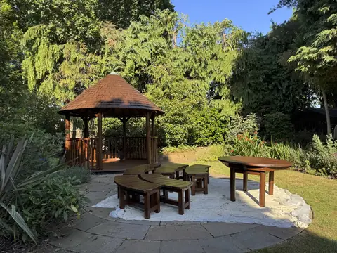 Circular gazebo with a brown varnished shingle roof and posts, with matching table and curved benches on the patio