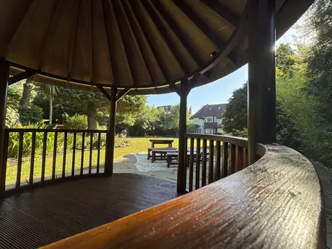 Curved varnished handrail and decking inside a gazebo, with a table and benches on the lawn beyond