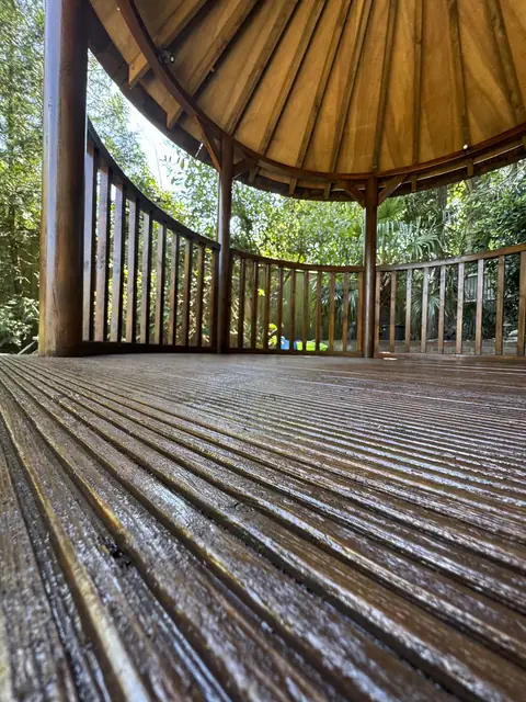Low view across varnished grooved decking inside a gazebo, with curved spindle rails and roof boards above