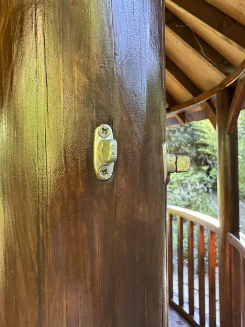 Close-up of a round gazebo post varnished in a deep brown, with a brass fixing and rails beyond