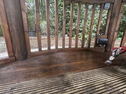 Grooved gazebo decking half coated in glossy brown varnish, a brush working along the boards and bare timber in front