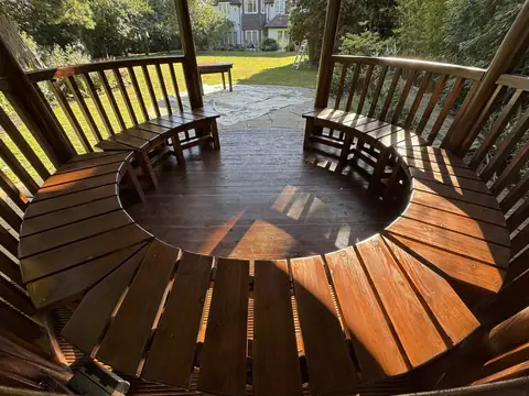 Ring of varnished curved benches inside the gazebo, seen from above, with the lawn and a ladder beyond