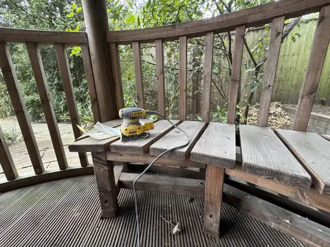 Weathered slatted bench inside the gazebo with an orbital sander and sanding sheets resting on it