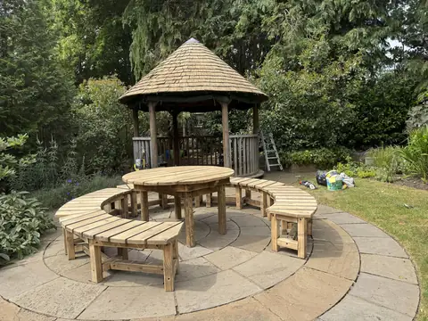 Round gazebo and its circular table and curved benches sanded back to pale bare timber on a stone patio
