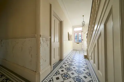 Victorian hallway with plaster stripped below the dado rail, a geometric tiled floor and a stained glass front door
