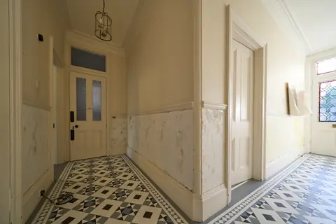Inner hallway with patchy stripped walls below the dado rail, panelled doors and a geometric tiled floor