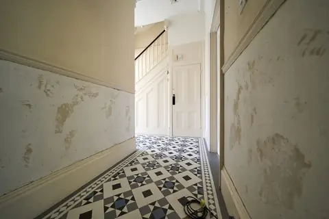 Hallway corridor with patchy stripped walls below the dado, leading to the staircase and under-stair door