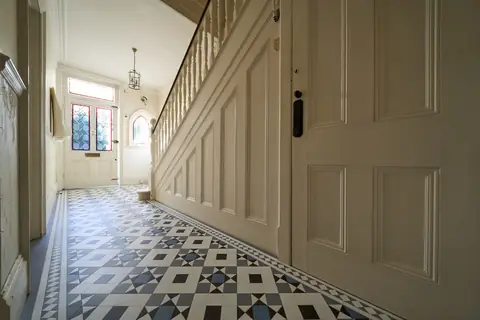 Ground floor hallway with cream stair panelling, spindles and a stained glass front door, before decorating