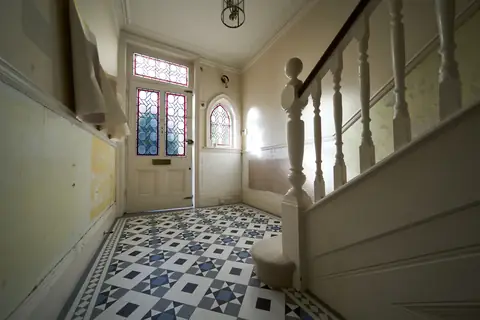 Entrance hall with bare plaster patches, a leaded stained glass front door, arched window and newel post