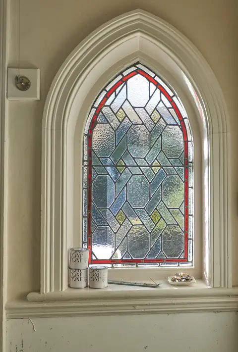 Gothic arched stained glass window with three Coat paint tins standing on the sill