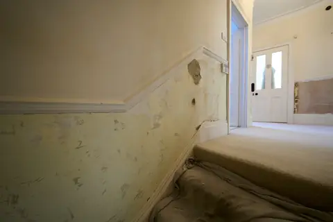 Stair wall with blown plaster and a stripped finish below the dado rail, with dust sheets on the stairs