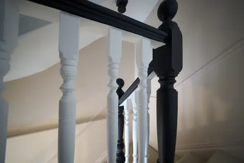 Close-up of white turned spindles beside a dark painted newel post and handrail