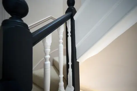 Close-up of a dark painted newel cap and handrail above white spindles and a stair string
