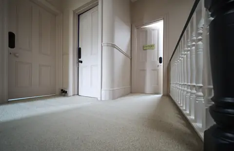 Top floor landing with pink doors and walls, a white balustrade and a dark newel post