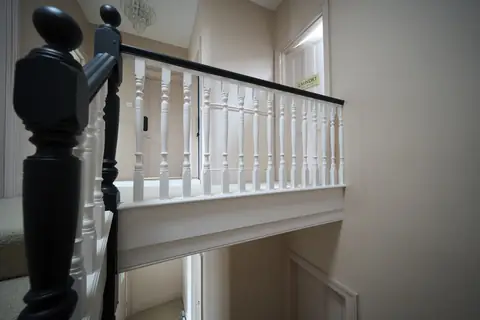 View across the stairwell to the top landing balustrade, with white spindles and a dark handrail