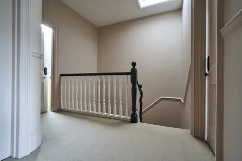 Top floor landing under a skylight with pink walls, white spindles and a dark newel post and handrail