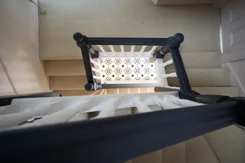 Looking down through dark handrails and white spindles to the tiled floor three storeys below