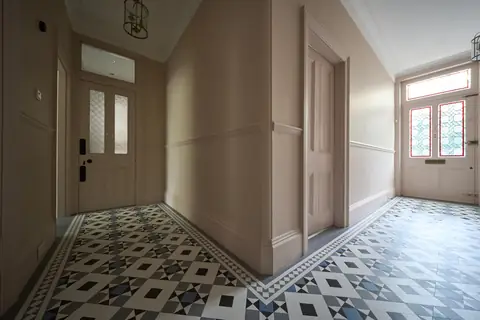 Inner hallway with light pink walls and woodwork, panelled doors and a geometric tiled floor