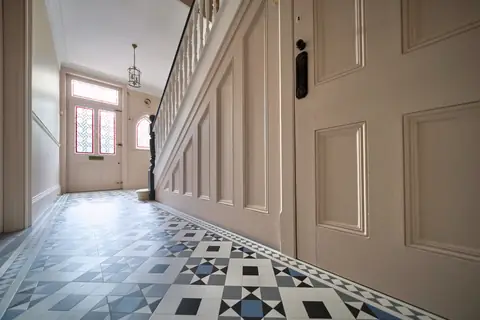 Ground floor hallway with pink walls and stair panelling, white spindles and a stained glass front door