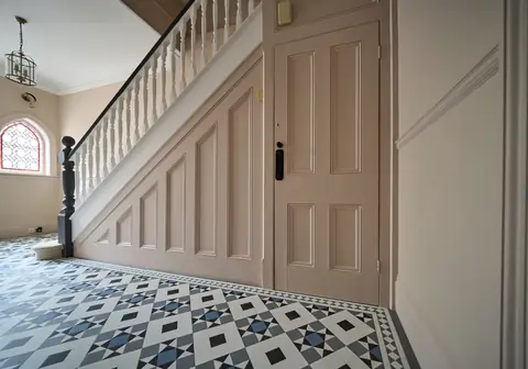 Panelled stair side and under-stair door painted light pink, above a geometric tiled floor